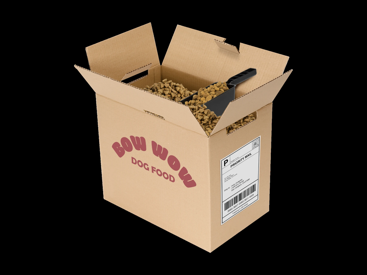 An open cardboard bulk box of dry pet food with a measuring scoop, printed BOW WOW DOG FOOD, on a black background